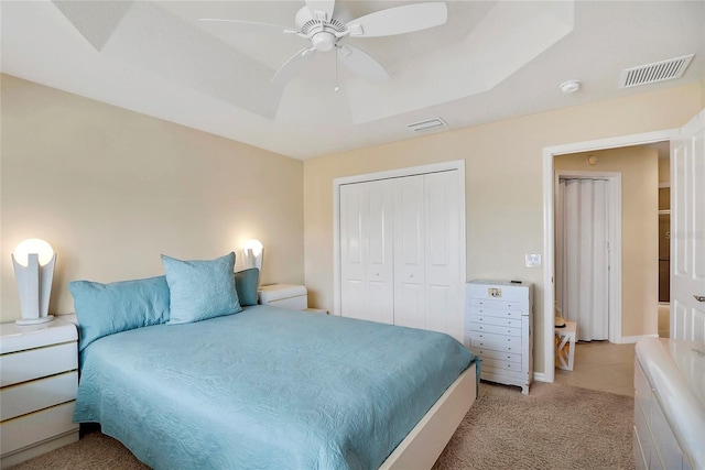 bedroom featuring light carpet, visible vents, a raised ceiling, a ceiling fan, and a closet