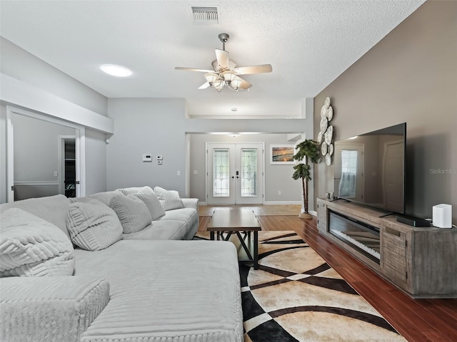 living room featuring a textured ceiling, ceiling fan, hardwood / wood-style floors, and french doors