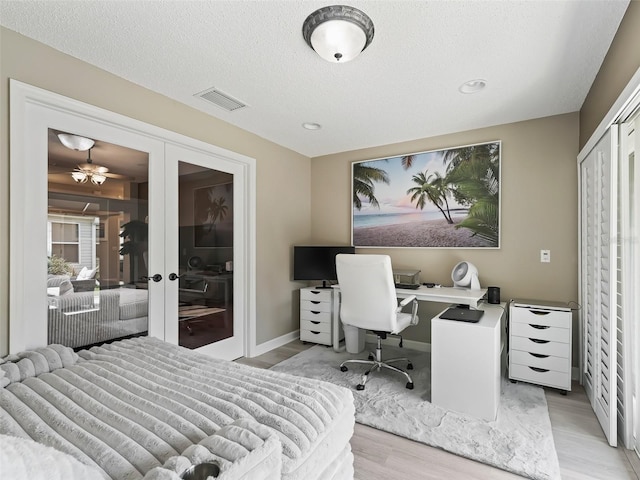 bedroom with light hardwood / wood-style floors, a textured ceiling, french doors, and a closet