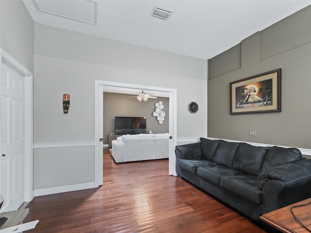 living room with a textured ceiling, dark wood-type flooring, and ceiling fan