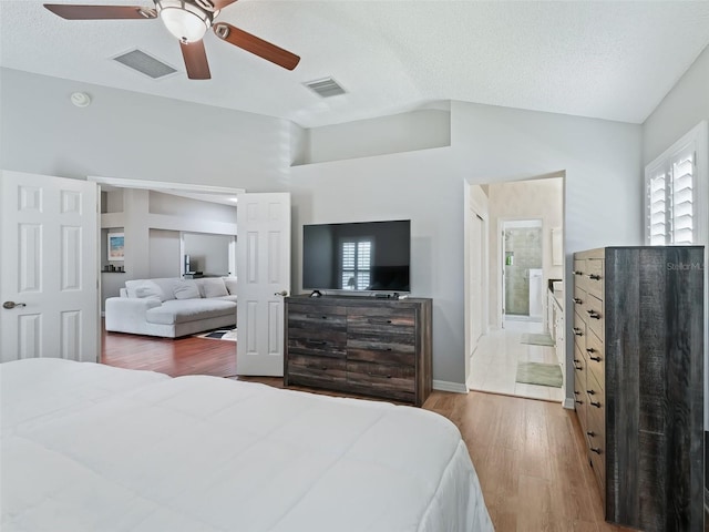 bedroom featuring hardwood / wood-style floors, a textured ceiling, ensuite bath, ceiling fan, and lofted ceiling