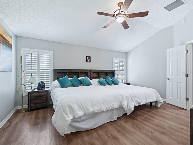 bedroom featuring wood-type flooring, vaulted ceiling, a textured ceiling, and ceiling fan