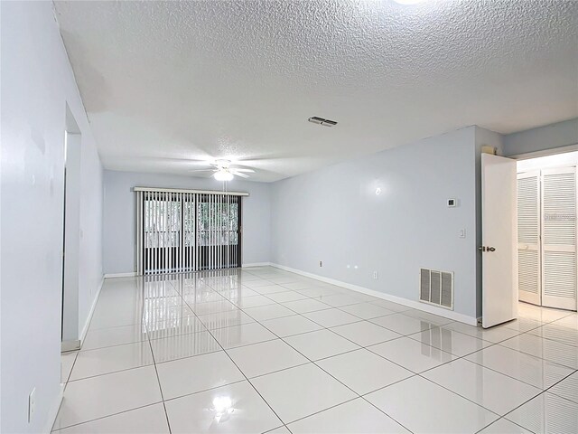 empty room with a textured ceiling, ceiling fan, and light tile patterned floors