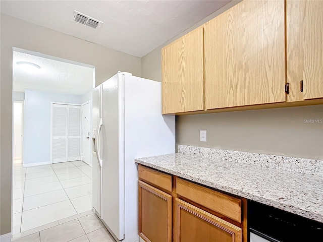 kitchen with light tile patterned floors, white fridge with ice dispenser, light stone countertops, and light brown cabinetry