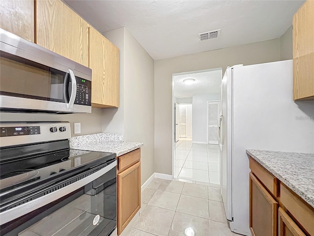 kitchen featuring light tile patterned floors, stainless steel appliances, light stone counters, and light brown cabinetry