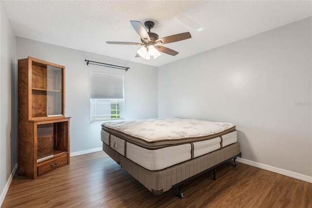 bedroom featuring dark hardwood / wood-style floors, ceiling fan, and a textured ceiling