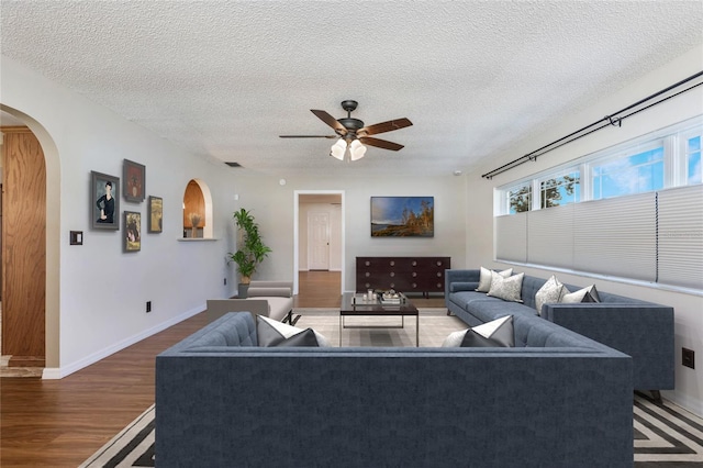 living room with a textured ceiling, ceiling fan, and dark wood-type flooring