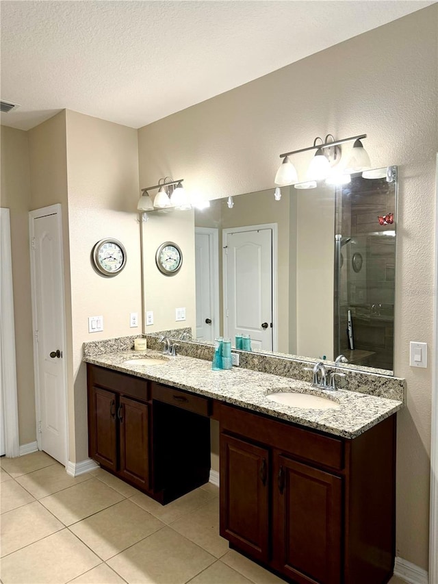 bathroom featuring a stall shower, double vanity, a sink, and tile patterned floors