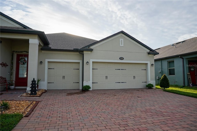 view of front of house featuring decorative driveway, a garage, a shingled roof, and stucco siding