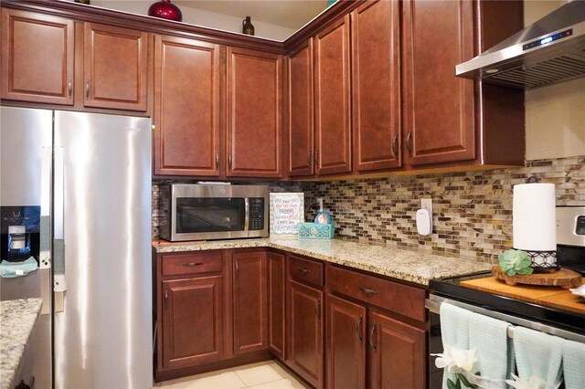 kitchen featuring light stone countertops, wall chimney exhaust hood, appliances with stainless steel finishes, and tasteful backsplash