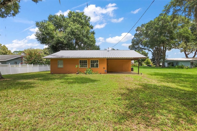 back of property with metal roof, a carport, a lawn, and fence