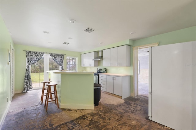 kitchen featuring a breakfast bar, stainless steel electric stove, white fridge, wall chimney exhaust hood, and white cabinets