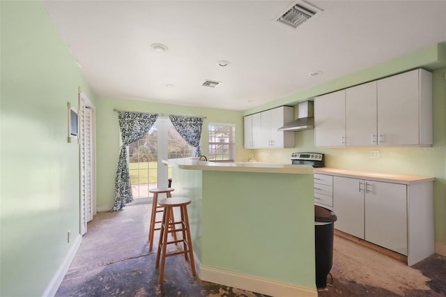 kitchen with a kitchen bar, a center island, wall chimney exhaust hood, and white cabinets