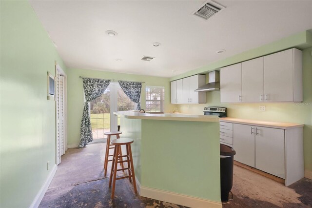 kitchen with visible vents, unfinished concrete flooring, stainless steel range with electric cooktop, wall chimney range hood, and white cabinetry