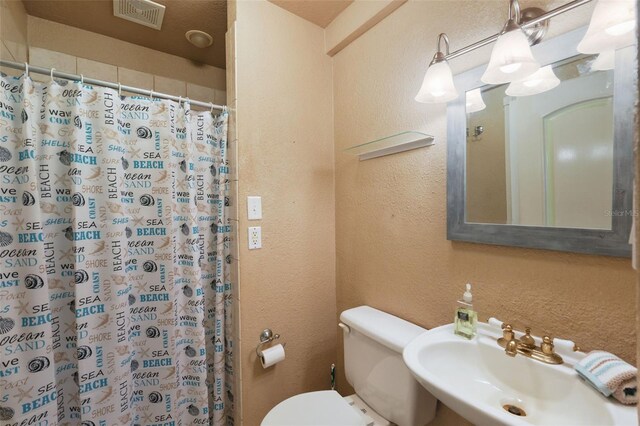 bathroom featuring visible vents, a shower with shower curtain, toilet, a textured wall, and a sink