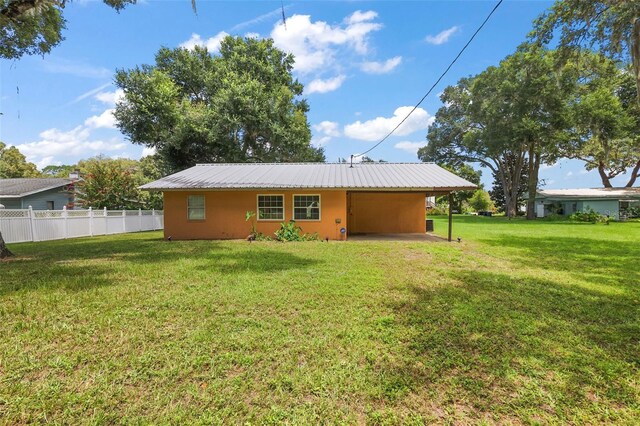 back of property with metal roof, an attached carport, a lawn, and fence