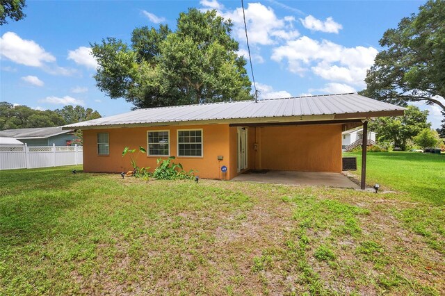 back of house featuring metal roof, fence, driveway, a lawn, and stucco siding