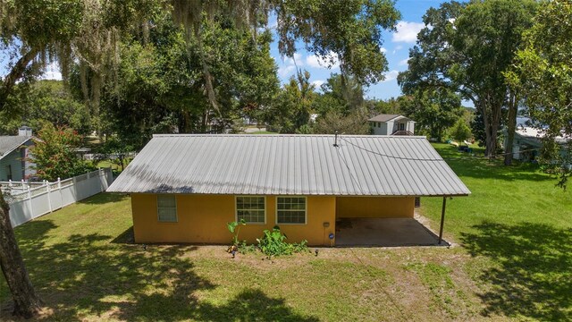 back of property with an attached carport, a yard, fence, and stucco siding