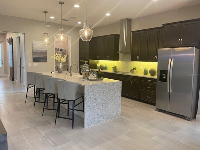 kitchen with a kitchen breakfast bar, wall chimney exhaust hood, decorative backsplash, stainless steel refrigerator with ice dispenser, and hanging light fixtures