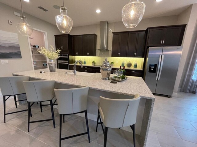 kitchen with wall chimney range hood, backsplash, appliances with stainless steel finishes, light tile patterned floors, and sink