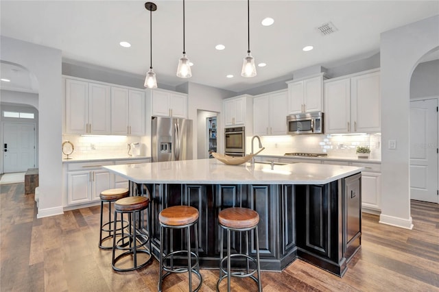 kitchen featuring white cabinetry, backsplash, an island with sink, appliances with stainless steel finishes, and hardwood / wood-style flooring