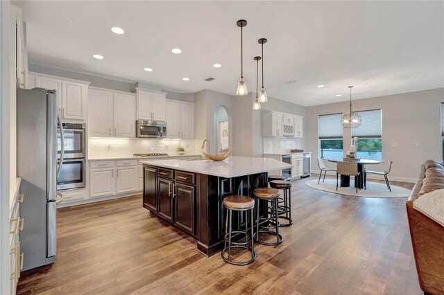 kitchen with decorative light fixtures, backsplash, appliances with stainless steel finishes, white cabinetry, and light wood-type flooring