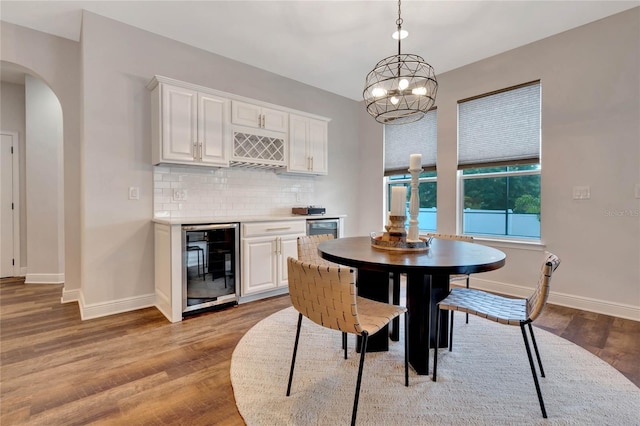 dining room with beverage cooler, a bar, arched walkways, and light wood-style flooring