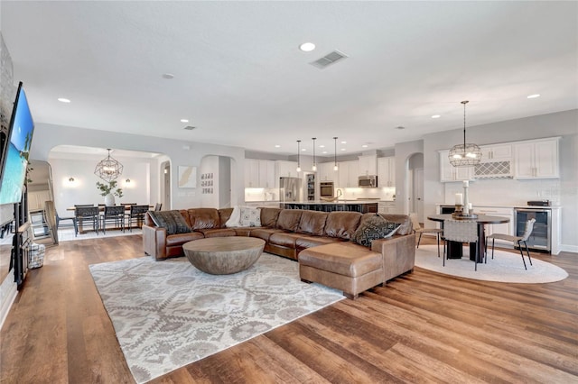 living room featuring wine cooler, arched walkways, visible vents, wood finished floors, and a chandelier