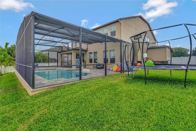 rear view of house with a patio, a lanai, a yard, stucco siding, and a trampoline