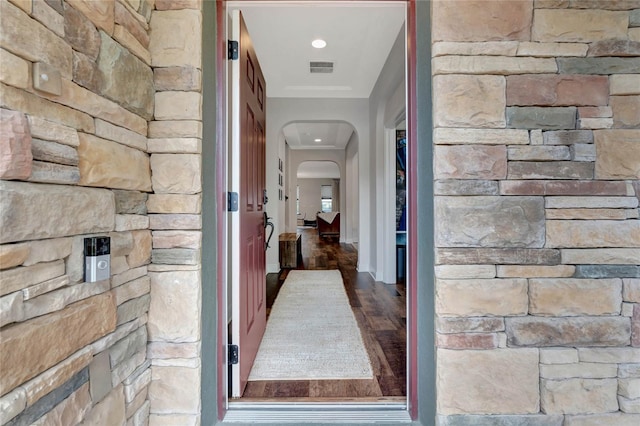 corridor with visible vents, arched walkways, and wood finished floors