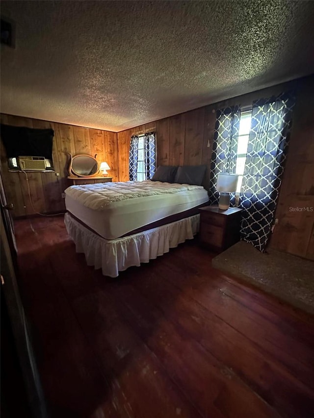 bedroom featuring dark wood-type flooring, multiple windows, wood walls, and a textured ceiling