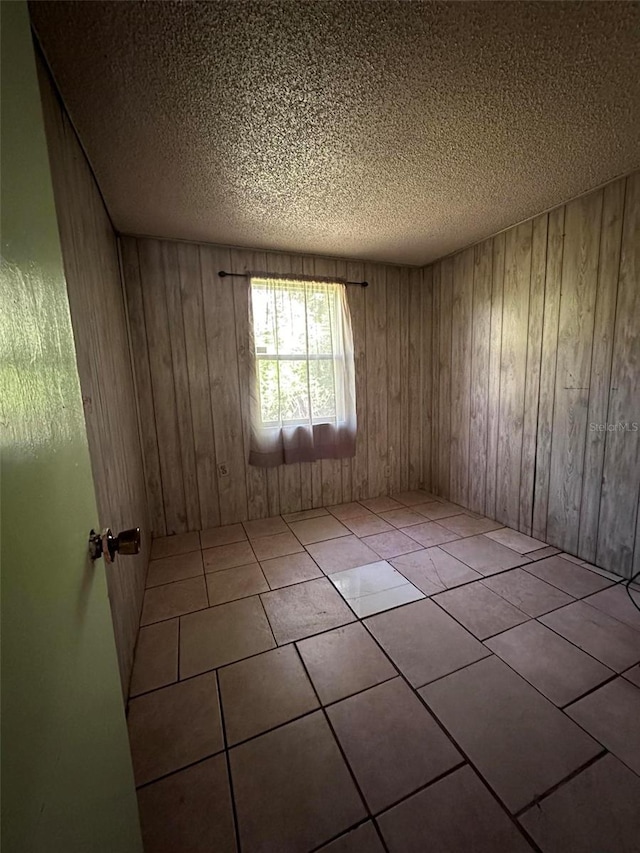 tiled empty room featuring wooden walls and a textured ceiling