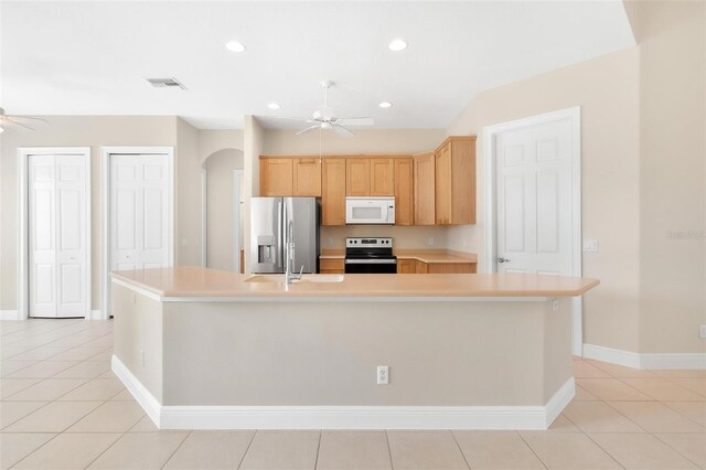 kitchen with stainless steel appliances, a center island with sink, light brown cabinetry, ceiling fan, and light tile patterned flooring