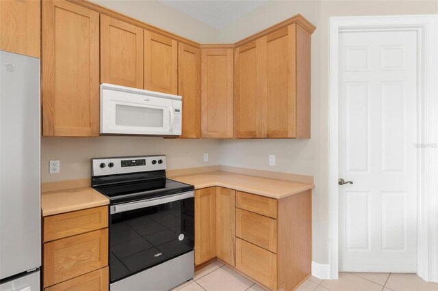 kitchen with light tile patterned floors, light brown cabinets, and white appliances