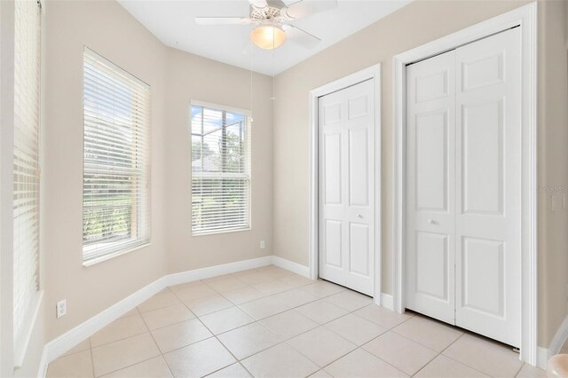 unfurnished bedroom featuring ceiling fan, two closets, and light tile patterned floors