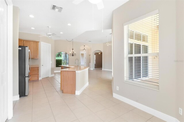 kitchen with a kitchen island with sink, ceiling fan with notable chandelier, sink, stainless steel fridge, and light tile patterned flooring