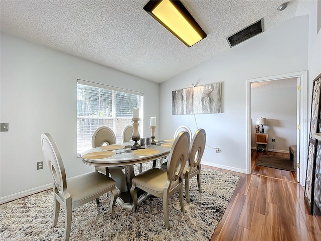 dining area featuring lofted ceiling, a textured ceiling, and dark hardwood / wood-style flooring