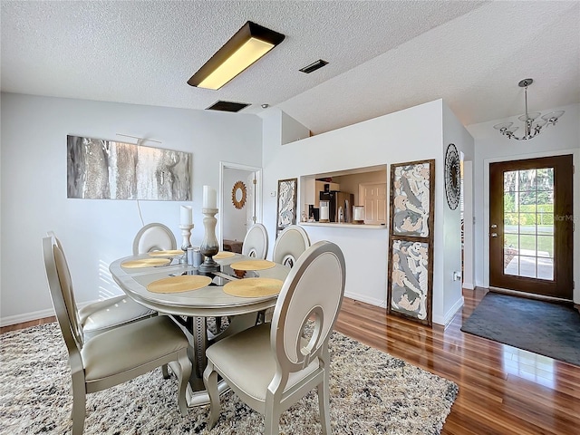 dining room featuring vaulted ceiling, a textured ceiling, an inviting chandelier, and dark hardwood / wood-style flooring