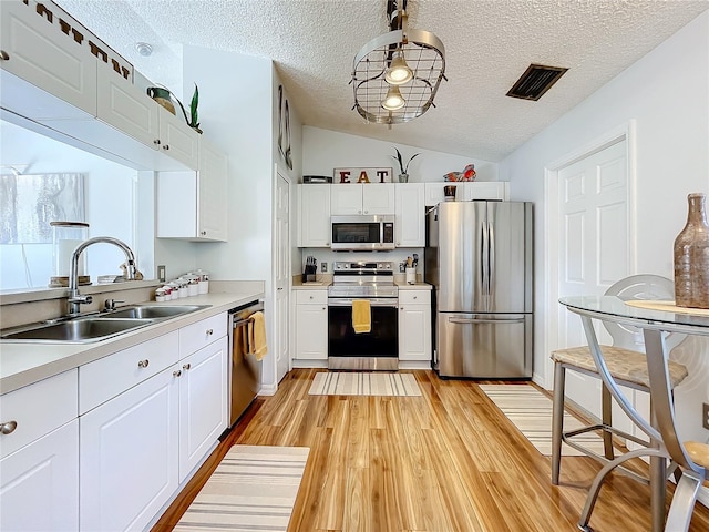 kitchen featuring appliances with stainless steel finishes, sink, white cabinetry, light hardwood / wood-style floors, and lofted ceiling