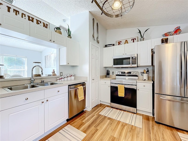 kitchen featuring white cabinets, appliances with stainless steel finishes, vaulted ceiling, light hardwood / wood-style flooring, and sink