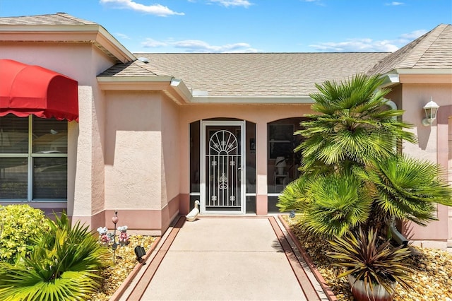 entrance to property with a shingled roof and stucco siding