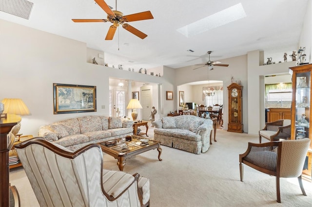 living area featuring arched walkways, a skylight, visible vents, light carpet, and ceiling fan with notable chandelier