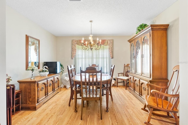 dining area with a chandelier, light wood finished floors, and a textured ceiling