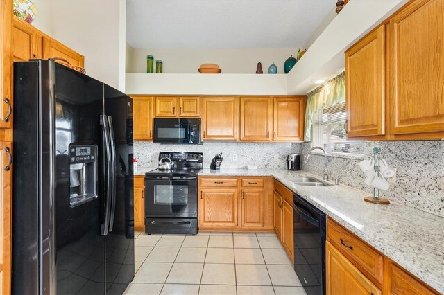 kitchen featuring backsplash, light tile patterned floors, light stone countertops, sink, and black appliances