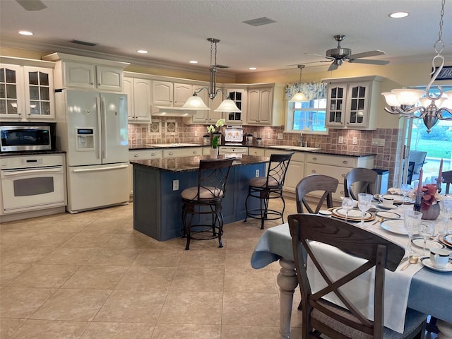 kitchen featuring dark stone counters, ceiling fan with notable chandelier, white appliances, pendant lighting, and a kitchen island