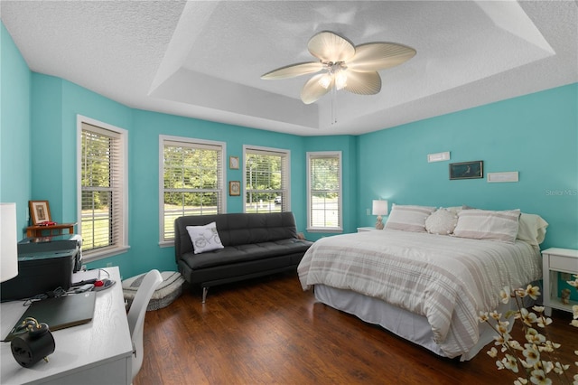 bedroom with a raised ceiling, multiple windows, ceiling fan, and dark hardwood / wood-style flooring