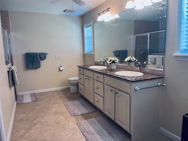 bathroom with a textured ceiling, vanity, a shower with door, tile patterned flooring, and toilet