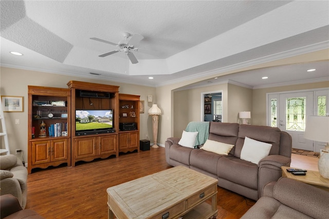 living room with ceiling fan, ornamental molding, dark wood-type flooring, and a tray ceiling