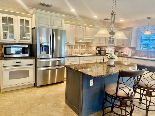 kitchen with decorative light fixtures, appliances with stainless steel finishes, white cabinets, a sink, and dark stone countertops