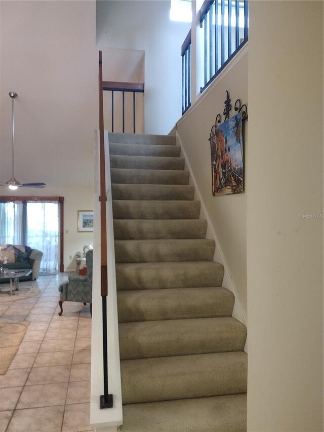 stairway with ceiling fan, a high ceiling, and tile patterned flooring